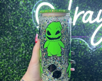 May include: A green glitter tumbler with a green and black character from the movie "The Nightmare Before Christmas" on the front. The tumbler has a green lid with a silver band.
