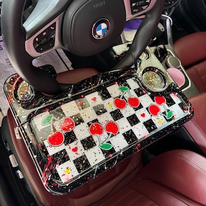Peut inclure: Un plateau à damier noir et blanc avec des cerises rouges et des paillettes dorées. Le plateau est fixé au volant d'une voiture.