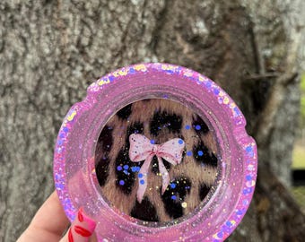 May include: Pink glitter ashtray with a leopard print and a pink bow inside.