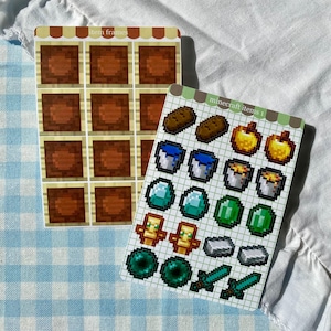 May include: Two sticker sheets featuring Minecraft graphics. One sheet displays twelve brown square item frames with a tan border. The second sheet contains various pixelated game items including golden apples, buckets, diamonds, emeralds, and swords.