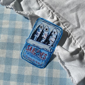 Könnte beinhalten: Blaue Sardinenbüchsen-Illustration mit drei Fischen im Inneren. Auf der Dose steht das Wort "SARDINES" und der Text "BY SHININGDALBIT". Der Hintergrund ist ein blau-weiß kariertes Muster.