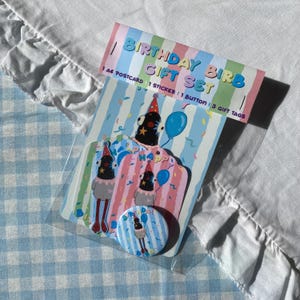 Könnte beinhalten: Ein Geburtstagsgeschenk-Set in einer transparenten Plastikhülle. Das Set enthält eine Postkarte, einen Aufkleber, einen Knopf und Geschenkanhänger. Die Verpackung hat ein gestreiftes Design mit den Worten "BIRTHDAY BIRB GIFT SET". Die Illustrationen zeigen einen Cartoon-Vogel mit Partyhut und Luftballon.