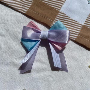 May include: A pastel blue, pink, and white bow with a satin finish. The bow is tied with a white ribbon.