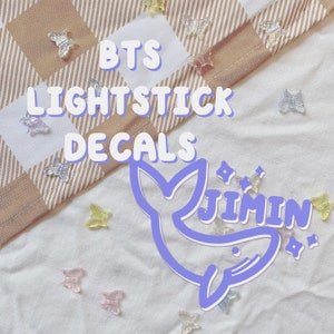 May include: Purple and white BTS lightstick decals featuring a whale with the word "Jimin" inside. The decals are on a white fabric background with small, colourful butterfly-shaped decorations.