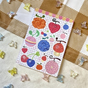 Könnte beinhalten: Ein Bogen Sticker mit verschiedenen bunten Teufelsfrucht-Designs aus dem Anime One Piece. Die Sticker sind auf weißem Hintergrund mit einem Gittermuster. Der Text "devil fruits" steht oben auf dem Bogen.