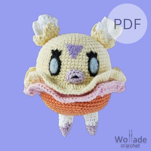 Op de afbeelding: Een gehaakt amigurumi-speelgoed in de vorm van een geel en oranje wezen met een roze rok. Het wezen heeft grote ogen, een kleine neus en een paarse driehoek op zijn voorhoofd. Het speelgoed is in de rechterbovenhoek met "PDF" gelabeld.