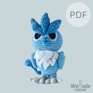 May include: A blue and white crocheted amigurumi toy of a bird-like Pokemon character with a spiky crest. The toy has black eyes and a white ruff. The image includes the word "PDF" in a white circle.