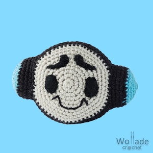 May include: A crocheted plush toy in the shape of a face with black eyes, a black mustache, and a smiling mouth. The toy is white with black and blue accents.