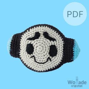 May include: Crochet pattern PDF for a smiling, white, black, and blue character with a round head and two small ears. The pattern is titled "Woll-ade Crochet".