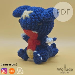May include: A handmade crochet plush toy of a blue creature with a red chest and yellow details. The toy has white teeth and small black eyes. The word "PDF" is in a white circle in the upper right corner.