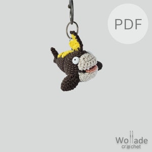 May include: Crochet amigurumi key chain of a brown and yellow Pokemon character with white eyes and a pink tongue. The keychain is attached to a silver key ring.