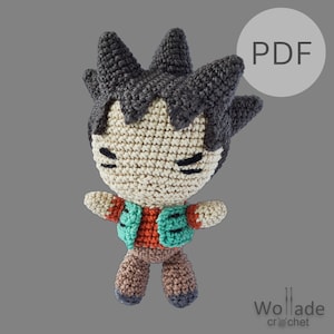 May include: Crocheted amigurumi toy of a cartoon character with brown hair, a red and green vest, and brown pants. The toy has a closed-eye expression and is standing with its arms outstretched. The image includes the text "PDF".