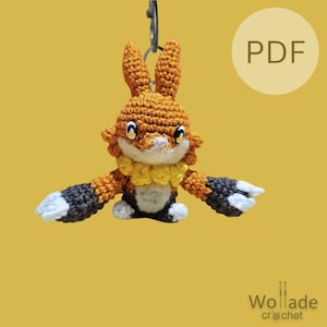 May include: A crocheted orange and black fox keychain with yellow accents. The keychain is hanging from a silver key ring. The image includes the text "PDF".
