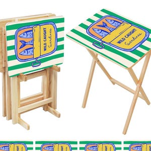 May include: A set of four folding TV trays with a sardine can design. The trays have a white background with green stripes and feature the text "WILD CAUGHT Sardines". The legs are made of natural wood.