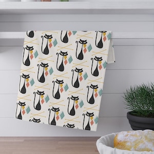 Puede incluir: Una toalla de cocina blanca con un patrón de gato negro. El gato sostiene una bola de hilo en sus patas. El hilo es en tonos de azul, rosa y amarillo. El fondo es blanco con una textura sutil.