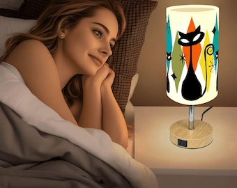 May include: A retro-style table lamp with a cylindrical shade featuring a black cat silhouette and colorful diamond shapes. The lamp has a wooden base and a chrome stem. The design includes orange, teal, and white accents, creating a mid-century modern aesthetic.