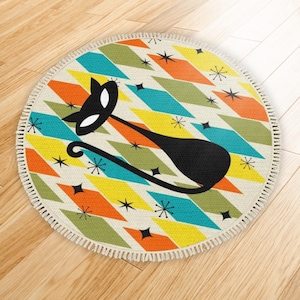 May include: Round rug with a mid-century modern design featuring a black cat silhouette. The rug has a cream-colored background with colorful diamond shapes in orange, teal, yellow, and green. Black starbursts are scattered across the surface, and the rug has a fringed edge.