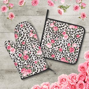 May include: A set of two kitchen accessories featuring a leopard print pattern with pink roses. The set includes a pot holder and an oven mitt.