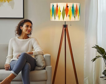 May include: A tripod floor lamp with a white lampshade featuring a geometric pattern of colorful diamonds and stars. The lampshade is made of fabric and has a wooden base.