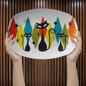 Peut inclure: Un plat de service ovale avec un design rétro. Le plat blanc présente des silhouettes de chats noirs et des éclats d'étoiles sur un fond de diamants colorés en rouge, jaune, turquoise, orange et vert. Un design amusant du milieu du siècle dernier.