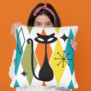 May include: A decorative pillow with a mid-century modern design. The pillow features a black cat silhouette against a white background with colorful geometric shapes in teal, orange, yellow, and green. The cat has a long tail and is centered on the pillow.