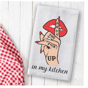May include: White kitchen towel with a red lip and a hand with a finger over the mouth. The text on the towel reads "Shut the F*ck Up in my kitchen".