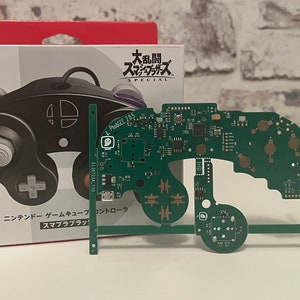 Könnte beinhalten: Ein schwarzer GameCube-Controller mit einem weißen Knopf und einer grünen Platine. Der Controller ist mit "Nintendo GameCube Controller" beschriftet und die Platine trägt den Text "Phabrix Z265".