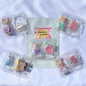 May include: Five clear plastic blister packs containing small flocked animal figurines and miniature accessories. The central pack features the text Mystery Critter with a graphic of a cake. The figures include rabbits and a bear wearing colorful clothing.