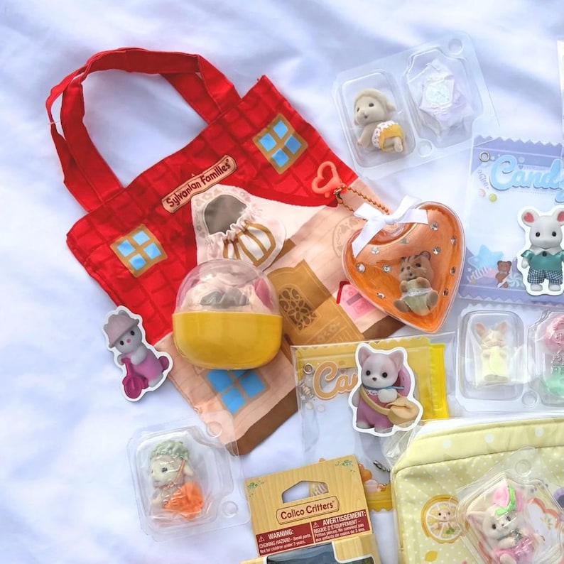 May include: A collection of Sylvanian Families toys and accessories. Includes a red house-shaped tote bag, miniature figures in clear packaging, and a heart-shaped ornament. The toys feature various animal characters and small details.