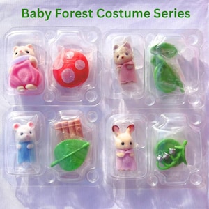 May include: A Baby Forest Costume Series set featuring four small animal figurines in individual clear plastic compartments. The set includes a pink-clad figure, a red mushroom, a tan figure, a green leaf, a white mouse, a brown fence, and a rabbit.