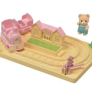 Pode incluir: Um conjunto de comboio de brinquedo em miniatura com um comboio rosa, uma carruagem de passageiros e uma esta&ccedil;&atilde;o. O conjunto inclui uma pequena figura de urso e uma pista amarela com um sinal de passagem de n&iacute;vel rosa. A esta&ccedil;&atilde;o tem um telhado rosa e relva verde.