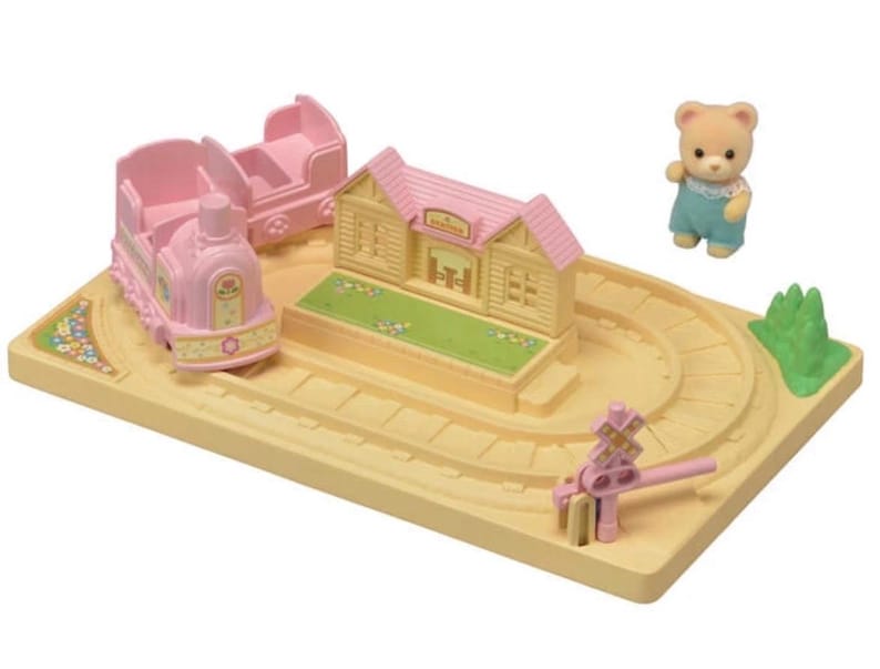Pode incluir: Um conjunto de comboio de brinquedo em miniatura com um comboio rosa, uma carruagem de passageiros e uma esta&ccedil;&atilde;o. O conjunto inclui uma pequena figura de urso e uma pista amarela com um sinal de passagem de n&iacute;vel rosa. A esta&ccedil;&atilde;o tem um telhado rosa e relva verde.