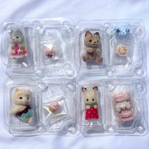 May include: Four clear plastic blister packs containing miniature flocked animal figurines and accessories. The set includes a gray cat, a brown tabby cat, a white cat, and a rabbit, accompanied by small items like a cupcake and a pink cradle.