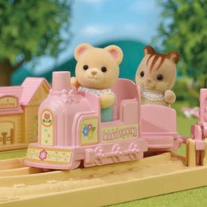 Pode incluir: Um comboio de brinquedo rosa com um urso e um gato como passageiros. O comboio tem a inscri&ccedil;&atilde;o "Baby Train" na lateral. O comboio est&aacute; sobre uma via de cor bege claro com uma esta&ccedil;&atilde;o amarela ao fundo. A cena &eacute; ao ar livre.