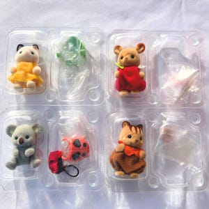 May include: A set of four flocked animal figurines in a clear plastic tray. The figures include a white cat in a yellow dress, a tan mouse in a red outfit, a gray koala, and a brown squirrel in an orange dress, plus a red ladybug accessory.
