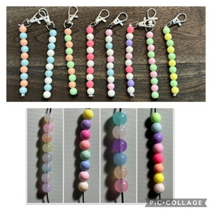 May include: A collection of beaded keychains in various pastel colors, including pink, blue, green, and yellow. Each keychain features a string of round beads attached to a silver-colored clasp.