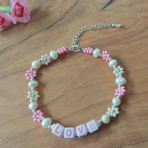 May include: A pink and white beaded bracelet with flower accents and the word "LOVE" spelled out in pink letters.
