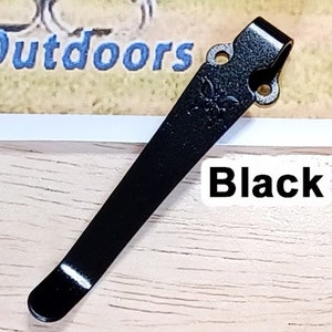 May include: Black metal pocket clip with two holes and a rounded tip.  The clip is designed to attach to a pocket or belt.