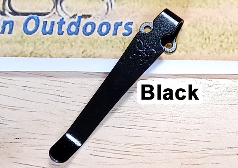 May include: Black metal pocket clip with two holes and a rounded tip.  The clip is designed to attach to a pocket or belt.