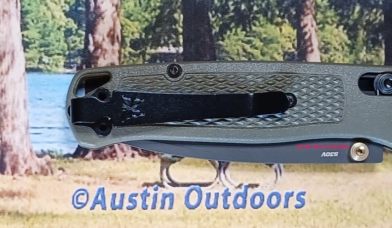 May include: A green pocket knife with a black clip and a textured handle. The knife has a black blade and a silver pocket clip. The knife is made by the company "ADCS".