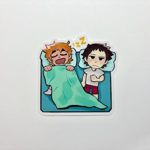 May include: A sticker featuring two cartoon characters in bed. One character is sleeping under a green blanket, while the other is awake. The sticker has a blue border and a white background.