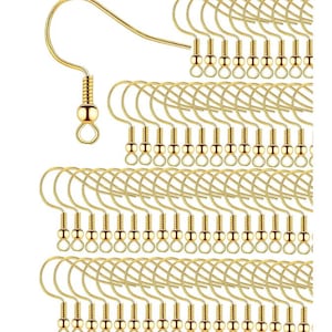 Può includere: Primo piano di ganci per orecchini color oro. I ganci sono disposti in file ordinate, mostrando il loro design curvo e una piccola sfera decorativa alla base. I ganci sono realizzati in un materiale metallico lucido, suggerendo un accessorio per la creazione di gioielli.