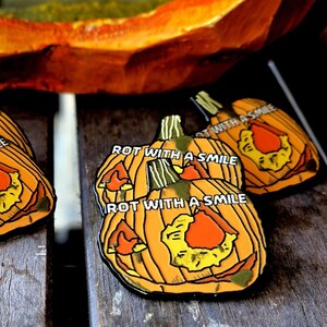 May include: Four enamel pins featuring a grinning jack-o'-lantern with the text "Rot with a smile" on each pin.