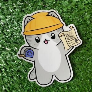 May include: A sticker featuring a cartoon cat wearing a yellow hard hat. The cat holds a blueprint and a blue tape measure. The cat is gray and white with black eyes and a pink mouth. The sticker is on a green surface.