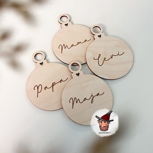 May include: Four wooden ornaments with the names "Mama", "Levi", "Papa", and "Maja" engraved on them. Each ornament has a small heart cut out at the top.