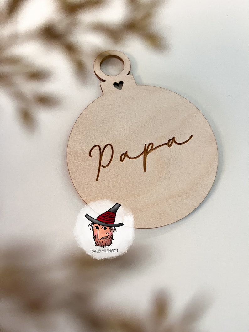 May include: A wooden Christmas ornament shaped like a bauble with the word "Papa" engraved on it. The ornament has a small heart cutout at the top.