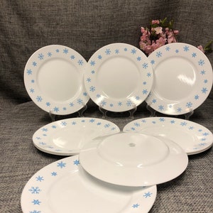 May include: A set of eight white ceramic dinner plates with a blue snowflake design around the rim.