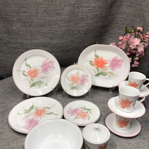 Puede incluir: Un juego de vajilla blanca con un diseño floral con flores rosas y naranjas. El juego incluye platos, cuencos, un azucarero y tazas y platillos.