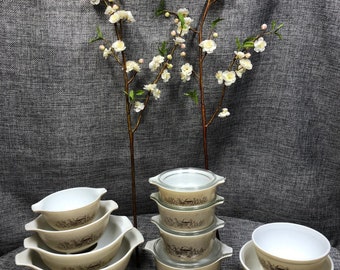 May include: A collection of beige and white glass bowls and lidded dishes featuring a brown pastoral scene print. The set includes four nesting bowls with side handles, a stack of four lidded round dishes, and two additional matching bowls.