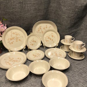 Puede incluir: Un juego de vajilla de cerámica blanca con un patrón floral. El juego incluye platos, cuencos y tazas.